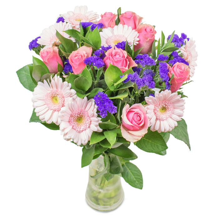 An artful floral display in a clear glass vase, this arrangement reflects the distinctive style of Mottingham floristry. At the centre are seven to nine pink roses in various stages of blooming-some tightly swirled, others gently opening-underscoring the timeless beauty of each stem. Surrounding these are five to seven pale pink Gerbera daisies, each with broad, comforting petals radiating from lighter, nearly white centres, bringing a sense of exuberance reminiscent of local gardens in full bloom near Elmstead Woods. Bright purple statice is thoughtfully interspersed, its small, textural flower clusters acting as jewels of the design. Rich green leaves form a verdant base, offering both depth and freshness, and visible stems in the vase allude to the bouquet's vibrant, just-picked condition. This arrangement, often selected for occasions like birthdays, anniversaries, or a thoughtful Mother's Day gift, is available for prompt delivery throughout Mottingham, courtesy of Flower Delivery Mottingham. Its joyous colours and lush form convey celebration, heartfelt affection, and a touch of local charm.